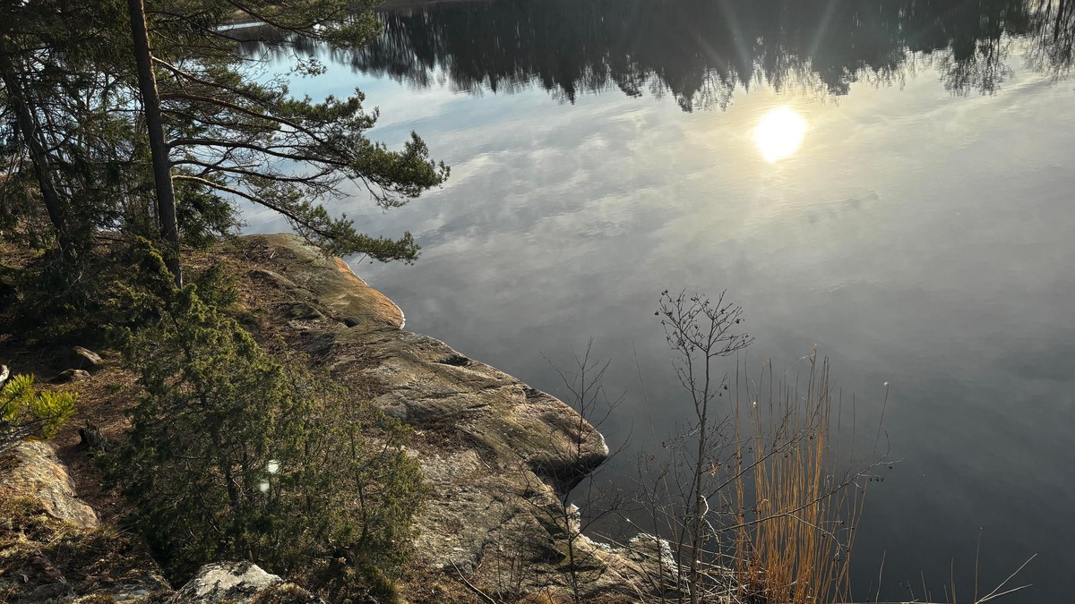 Photo of the sun and sky taken from a cliff, with the lower part to the cliff bordering the water in the left corner. Making a slight optical illusion. 